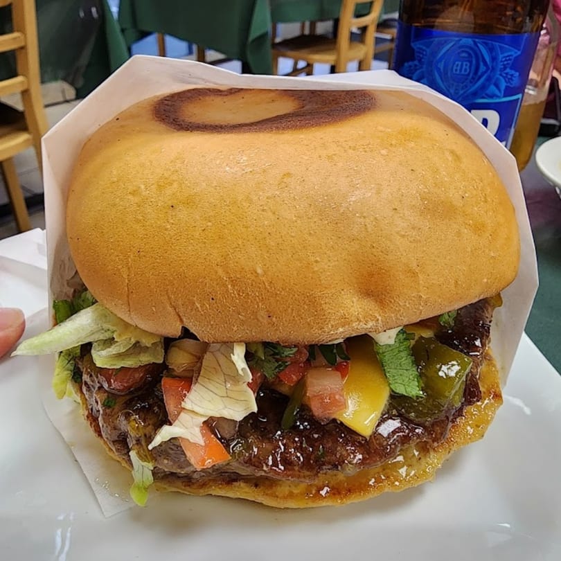 A Green Chile House burger with lettuce, tomato, and green chile, served with a beer.