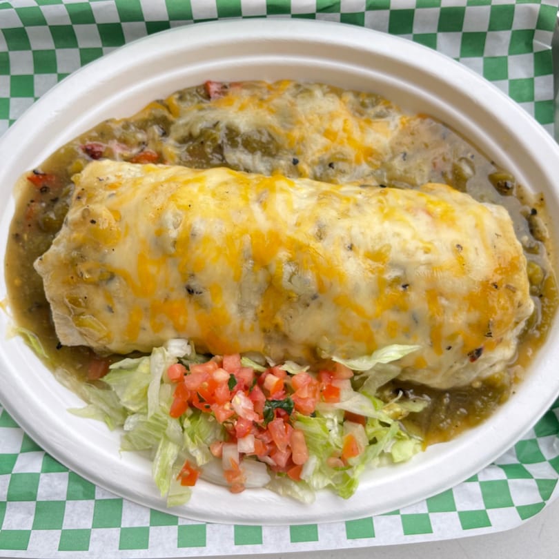 A Green Chile House burrito smothered in green chile sauce and melted cheese, with a side of lettuce and pico de gallo.