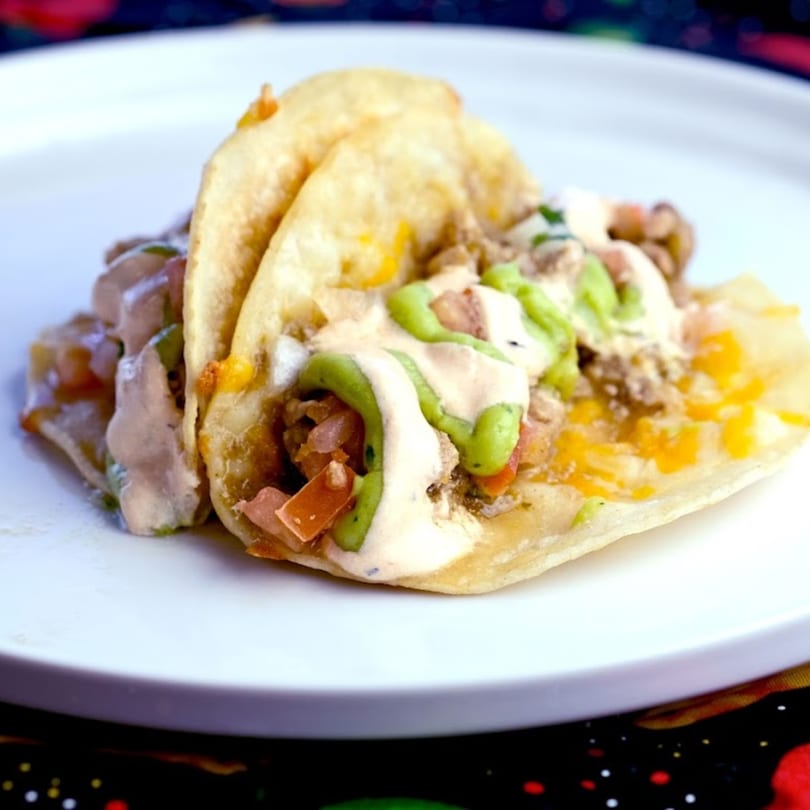 Two Green Chile House tacos with meat, cheese, and sauces on a white plate.